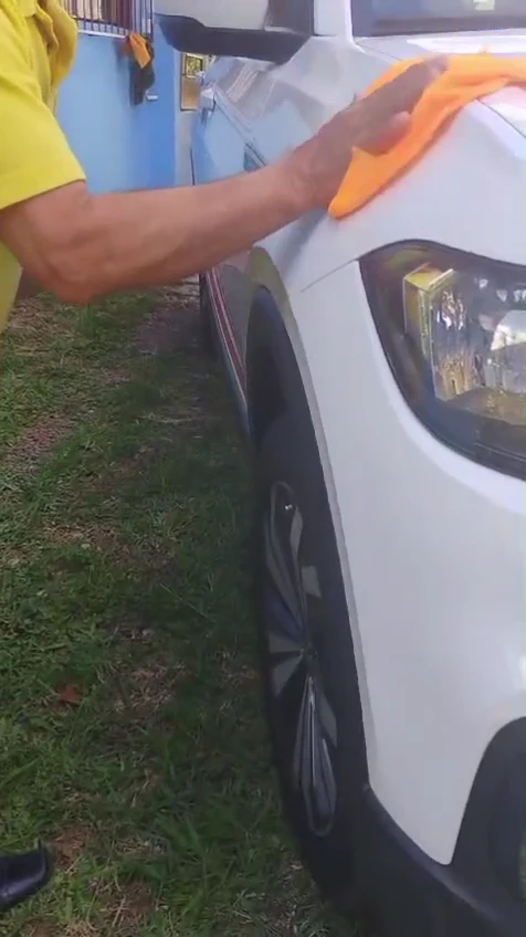 Toalha de microfibra laranja secando a resina no para-lama dianteiro de um carro branco